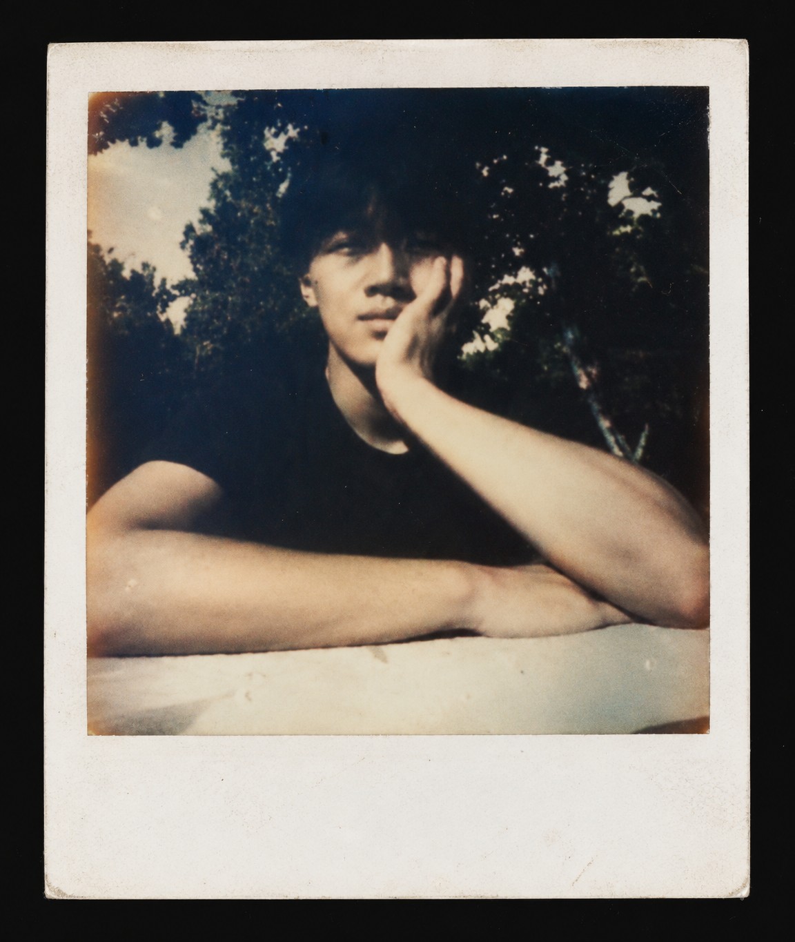 Polaroid-style portrait of Jeremy Shi resting his face on his hand beneath the trees.