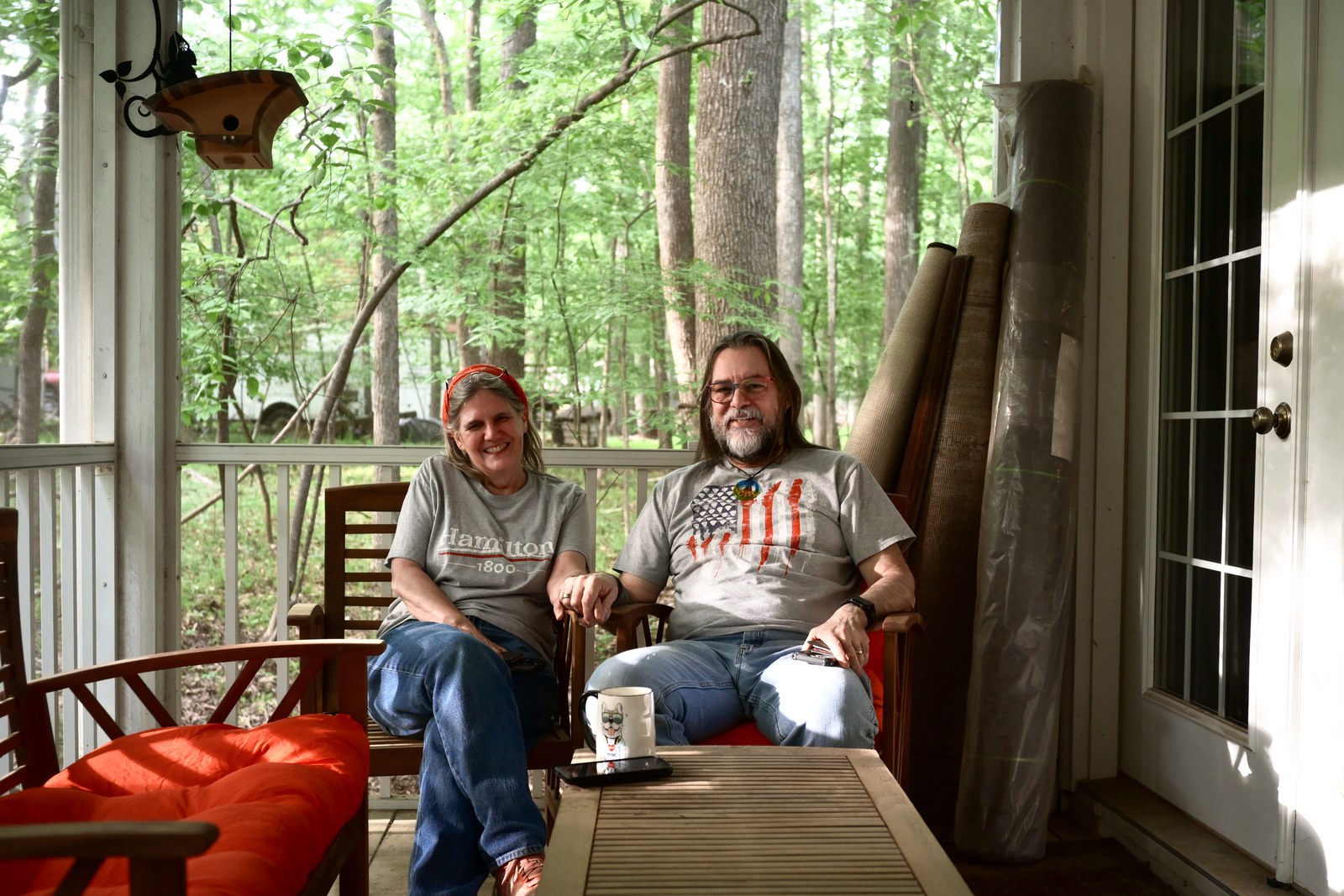 Two people sit together on a screened porch overlooking a green woodland.