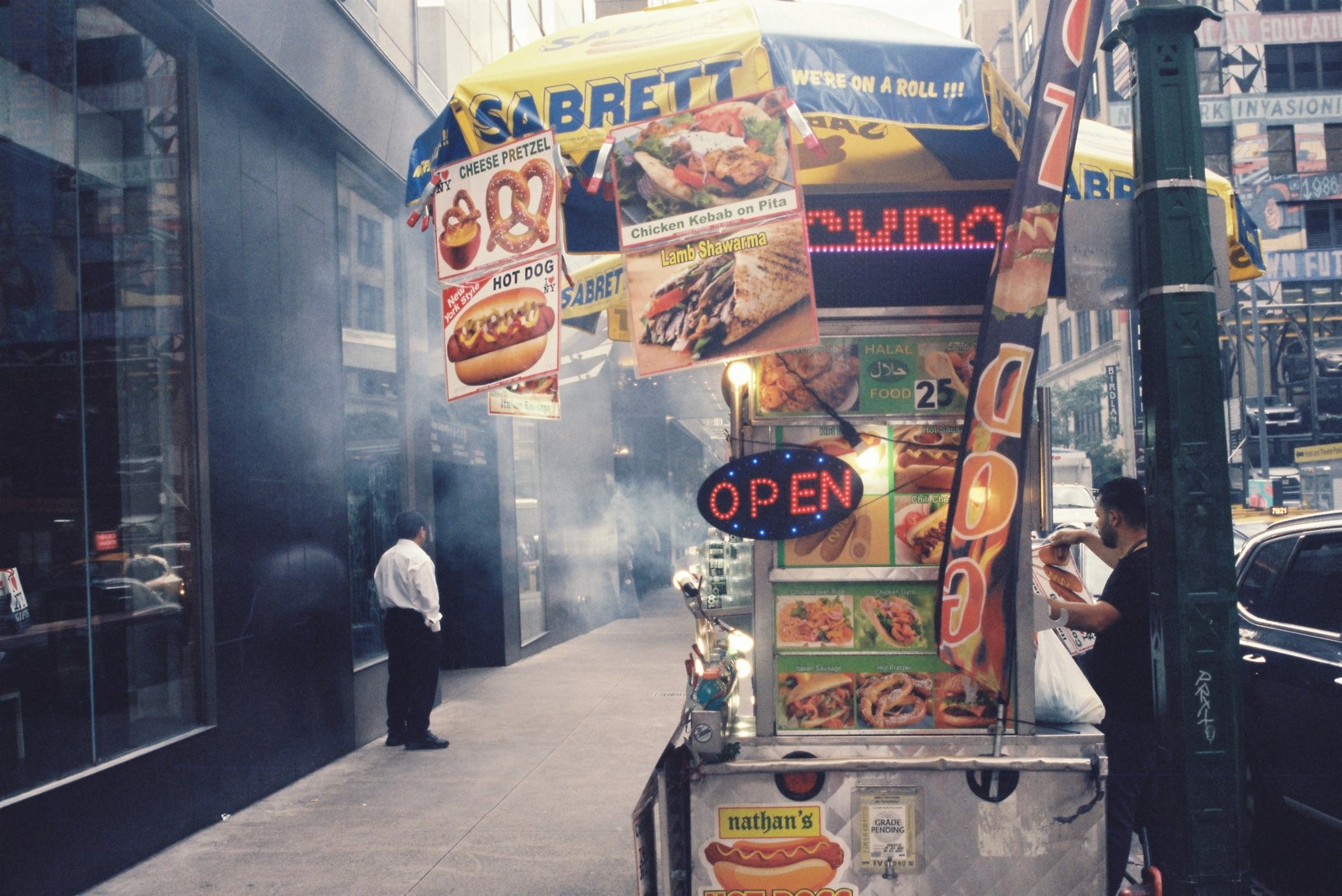 A street food cart surrounded by steam and storefronts.
